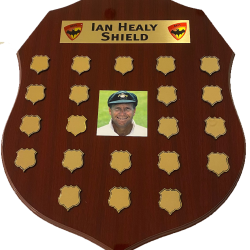 The Ian Healy Shield. Dark brown wooden sheld with 20 places to engrave annual match results. Has a phto of Ian Healy in the centrer of the shiield.