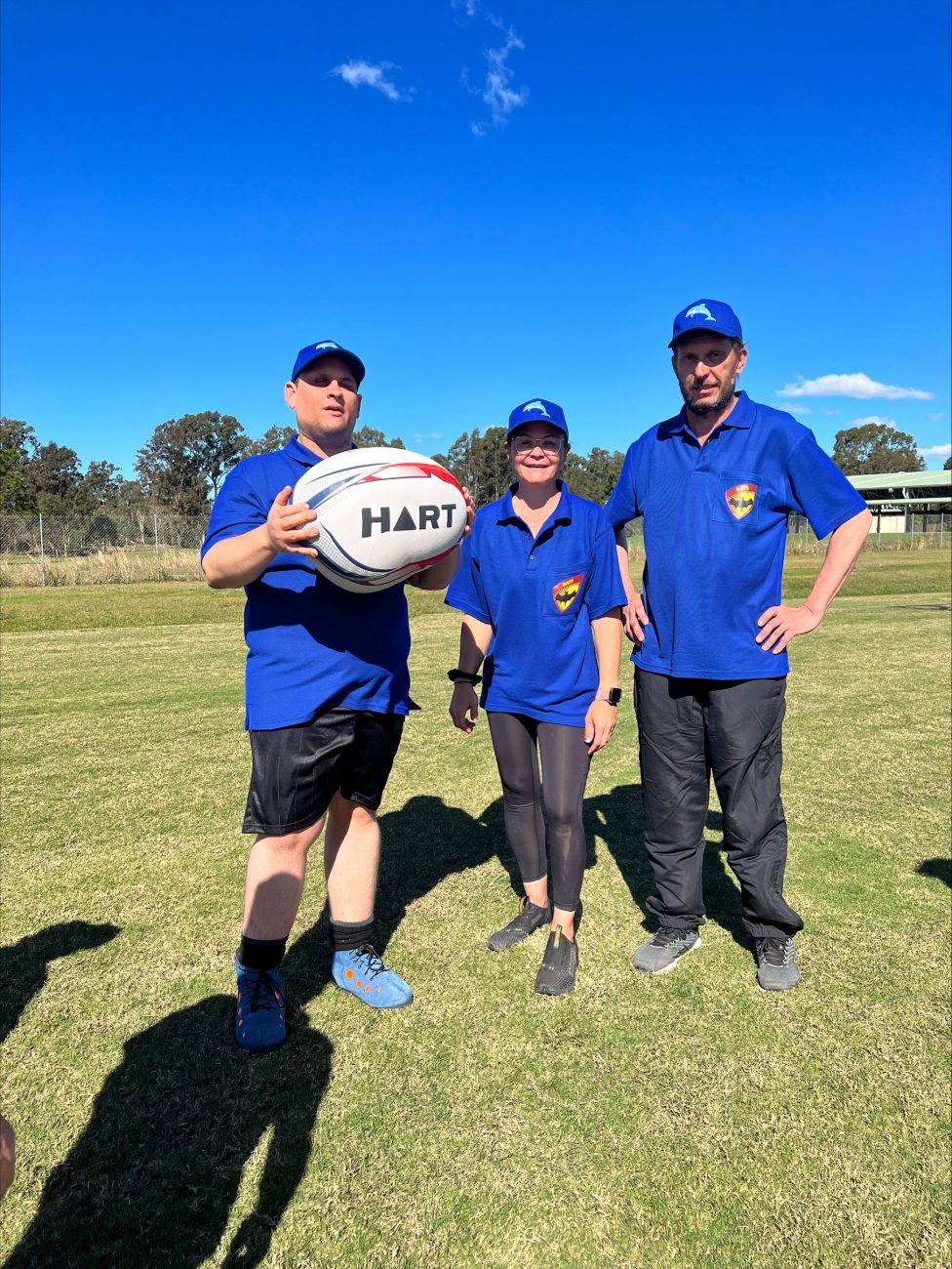 A photo of three Blue Dolphins Team members: Brendon (blind), Julie (very low vision), and Paul (full sight) with the very large ball used in Beep Tag. All proudly wearing their Blue uniforms.