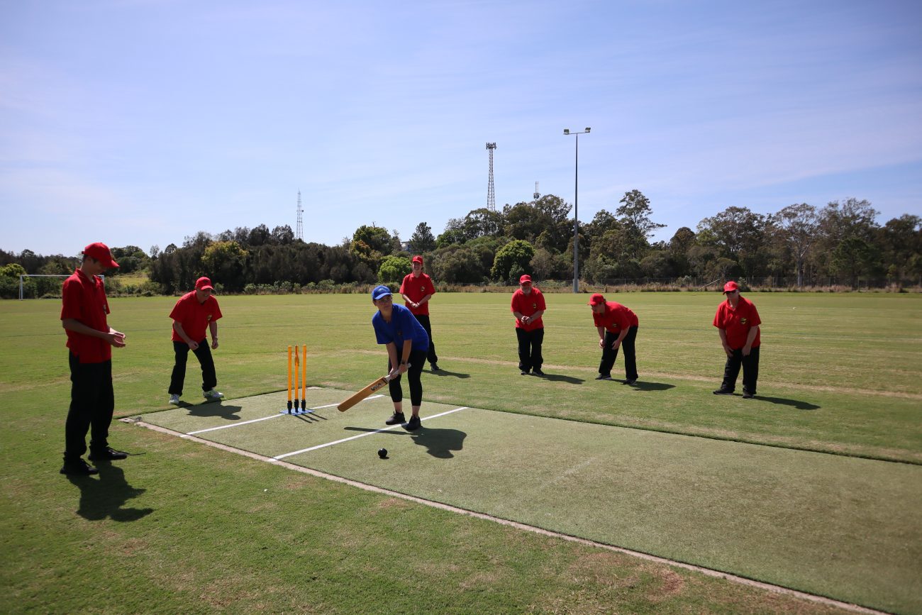Julie, captain of the Blue Dolphins team, is about to hit the new black beeping cricket ball out to the boundary. Julie, wearing the blue dolphin’s uniform, is surrounded by Red Dragons fields hoping to cut off the ball.