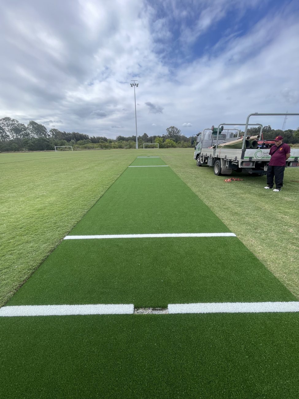 A photo of the new cricket pitch with dark grreen synthetic surface and bright white inlay lines.